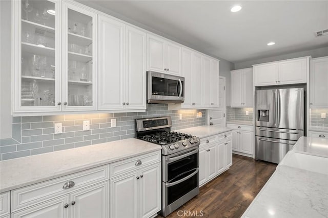 kitchen featuring light stone counters, white cabinets, stainless steel appliances, and dark wood-type flooring