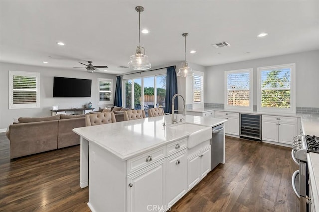 kitchen with beverage cooler, a center island with sink, a sink, stainless steel appliances, and dark wood-type flooring