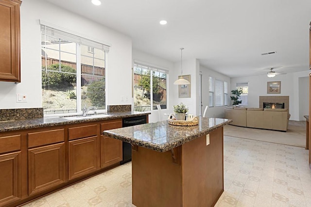 kitchen featuring a center island, a tiled fireplace, black dishwasher, brown cabinetry, and a sink