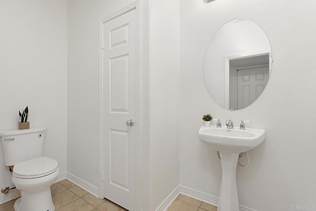 half bathroom with tile patterned floors, toilet, baseboards, and a sink