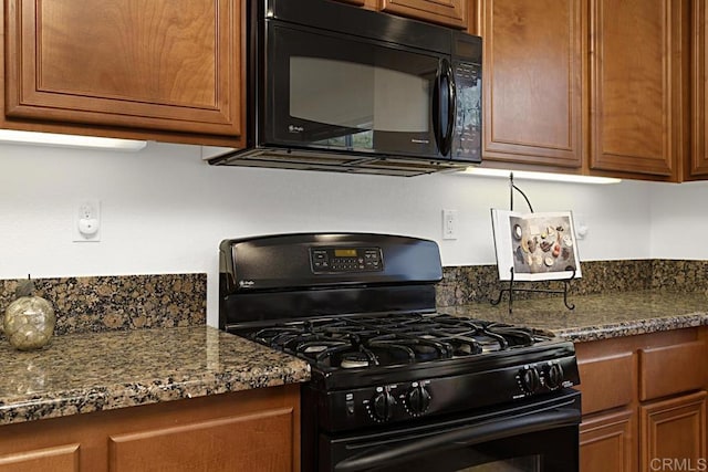 kitchen featuring brown cabinets, black appliances, and dark stone counters