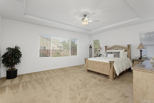 bedroom with a tray ceiling, light colored carpet, and baseboards