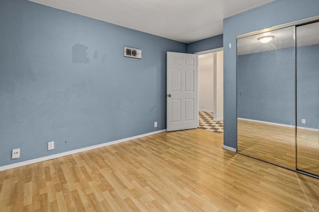 unfurnished bedroom featuring wood finished floors, a closet, and baseboards