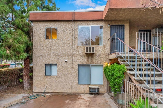 view of building exterior with stairway, a wall mounted air conditioner, and central AC