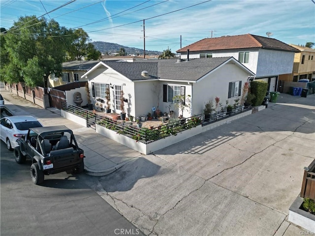 view of front facade with a fenced front yard, stucco siding, and roof with shingles