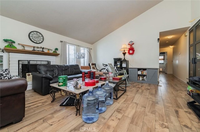 living room with a brick fireplace, light wood finished floors, and high vaulted ceiling