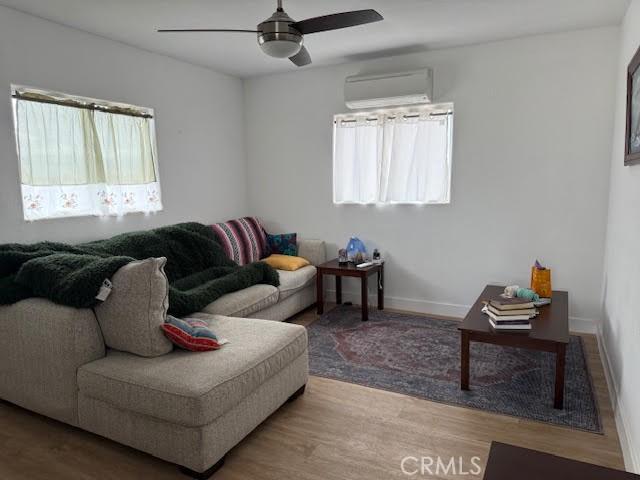 living area featuring ceiling fan, wood finished floors, baseboards, and a wall mounted AC