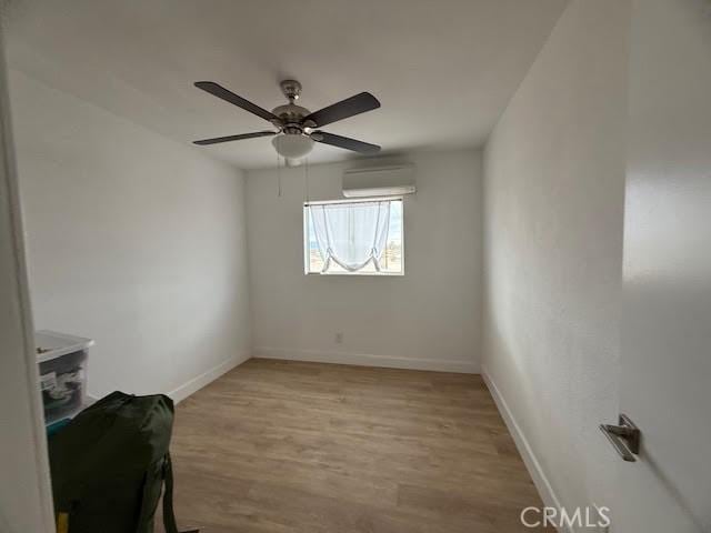 empty room with ceiling fan, light wood-type flooring, a wall mounted AC, and baseboards