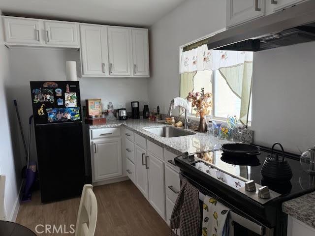 kitchen featuring freestanding refrigerator, a sink, under cabinet range hood, range with electric stovetop, and white cabinetry