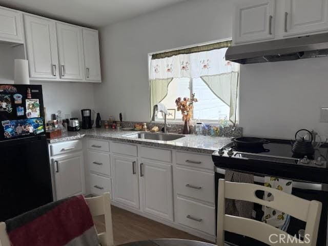 kitchen featuring freestanding refrigerator, a sink, light wood-style floors, under cabinet range hood, and white cabinetry