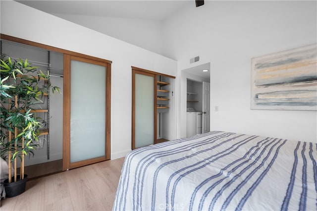 bedroom with visible vents, two closets, high vaulted ceiling, wood finished floors, and separate washer and dryer