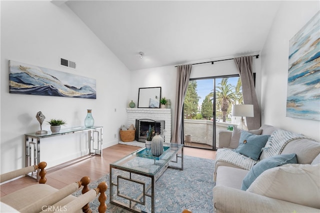 living room featuring visible vents, high vaulted ceiling, wood finished floors, a fireplace, and baseboards