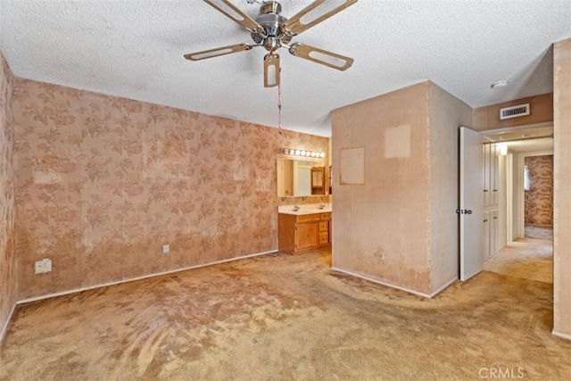 unfurnished bedroom with visible vents, a textured ceiling, connected bathroom, light colored carpet, and ceiling fan