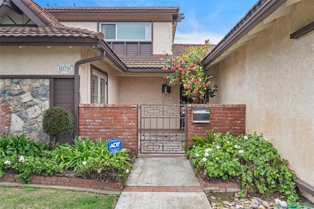 property entrance featuring a tiled roof, stucco siding, brick siding, and a gate