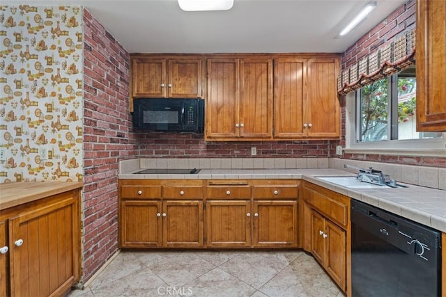 kitchen with light tile patterned floors, brown cabinetry, brick wall, a sink, and black appliances