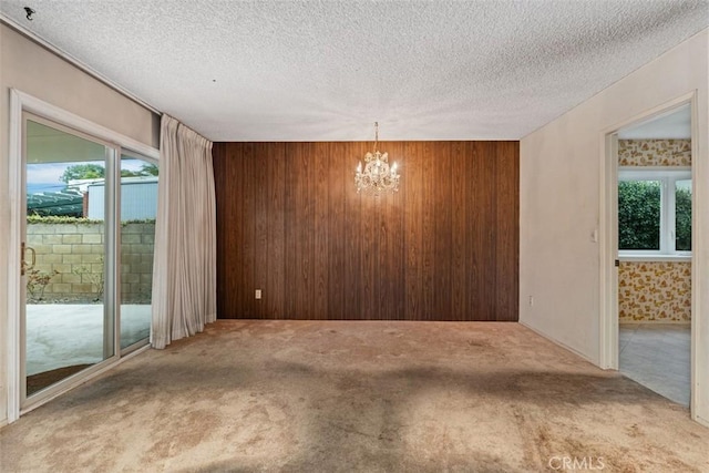 spare room with a chandelier, wooden walls, a textured ceiling, and carpet