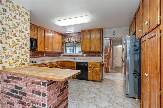 kitchen featuring black appliances, a sink, a peninsula, brown cabinetry, and decorative backsplash