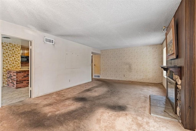 unfurnished living room with visible vents, a textured ceiling, a fireplace, and carpet flooring