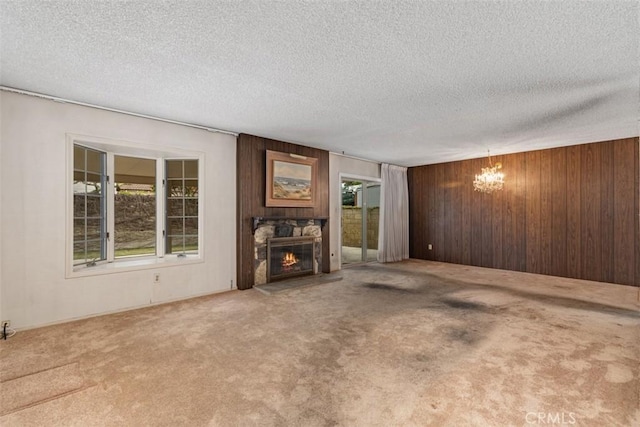 unfurnished living room with a notable chandelier, wood walls, a fireplace, and carpet floors