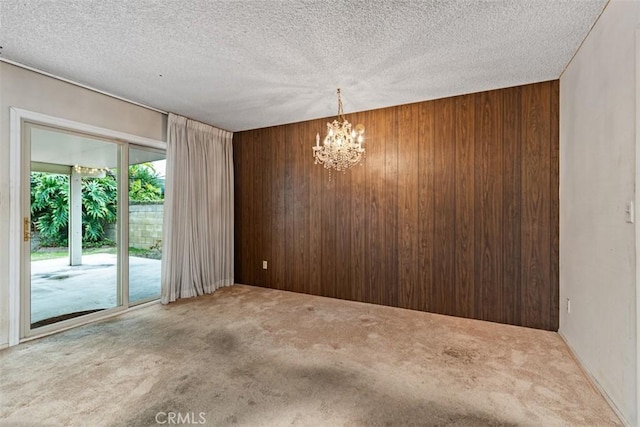 carpeted empty room featuring a textured ceiling, wooden walls, and a chandelier