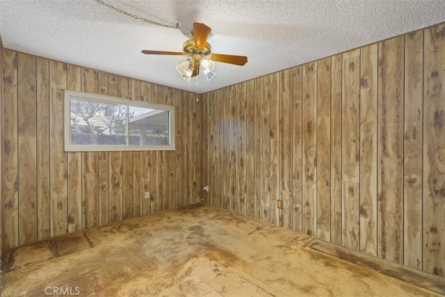 spare room featuring wooden walls, a textured ceiling, a ceiling fan, and carpet floors