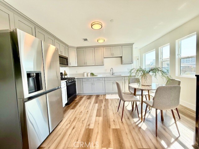 kitchen featuring stainless steel appliances, gray cabinetry, a sink, and light wood-style flooring