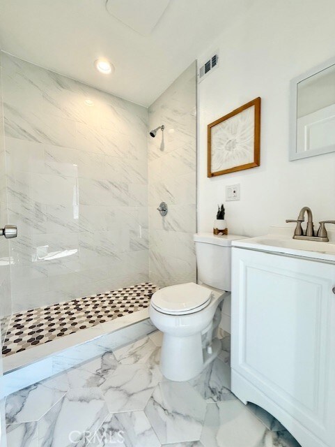 bathroom featuring a tile shower, vanity, toilet, recessed lighting, and visible vents
