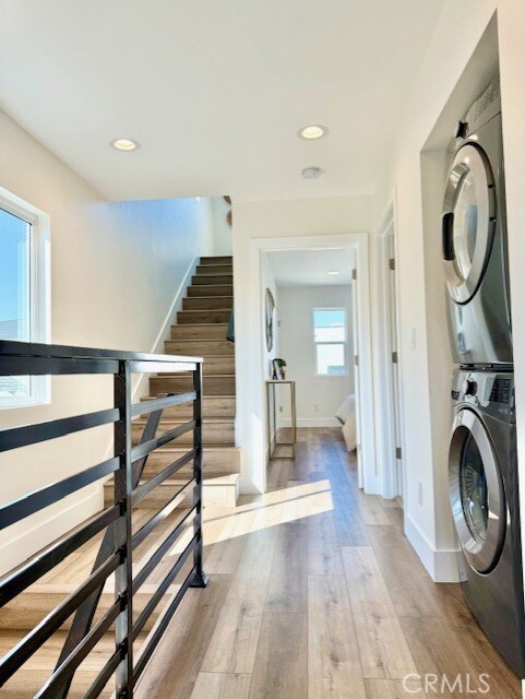 laundry room featuring laundry area, wood finished floors, stacked washer / dryer, baseboards, and recessed lighting