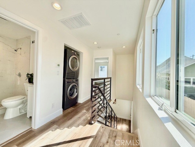hall featuring an upstairs landing, stacked washing maching and dryer, visible vents, and wood finished floors