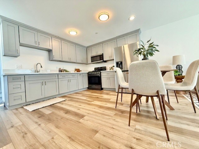 kitchen featuring light countertops, gray cabinets, a sink, light wood-style flooring, and stainless steel appliances