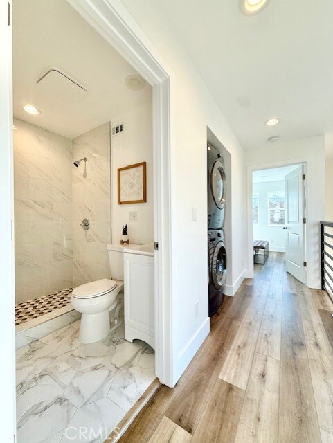full bathroom featuring stacked washer and dryer, wood finished floors, toilet, recessed lighting, and a tile shower