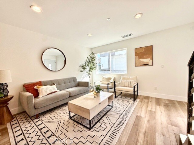 living room featuring visible vents, light wood-style flooring, and baseboards