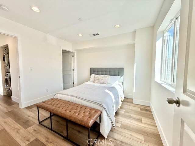 bedroom with visible vents, stacked washer / dryer, baseboards, recessed lighting, and light wood-style flooring