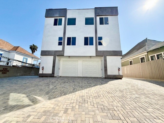 back of house featuring decorative driveway, an attached garage, fence, and stucco siding