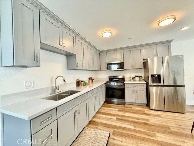 kitchen featuring light countertops, gray cabinets, a sink, light wood finished floors, and appliances with stainless steel finishes