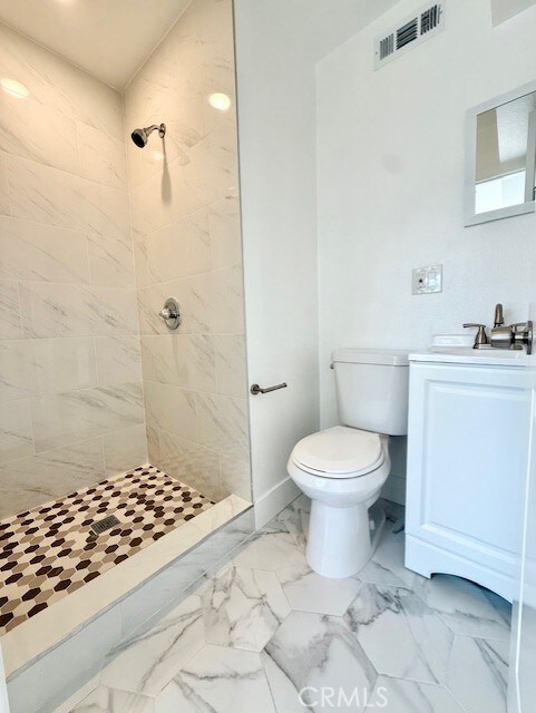 full bathroom with toilet, visible vents, tiled shower, and vanity