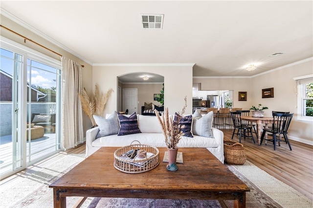 living room featuring wood finished floors, crown molding, arched walkways, and visible vents