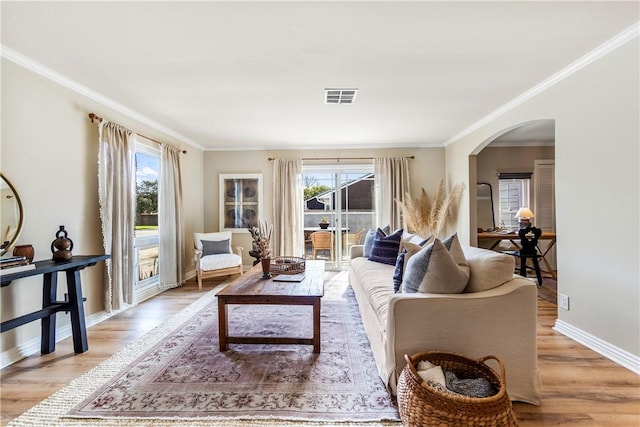 living area with wood finished floors, visible vents, baseboards, arched walkways, and crown molding