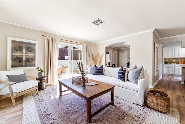 living room with arched walkways, visible vents, light wood finished floors, and ornamental molding