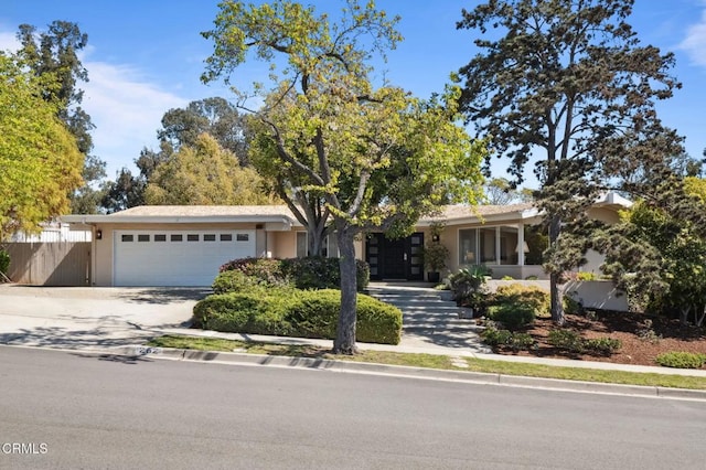 view of front facade featuring concrete driveway, an attached garage, and fence