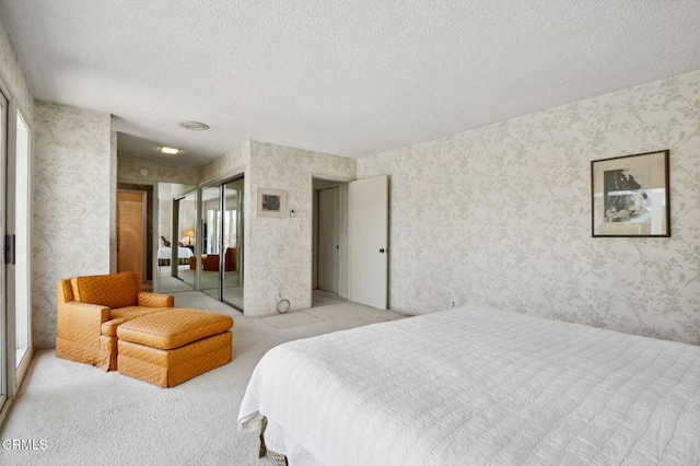 bedroom featuring a closet, light colored carpet, a textured ceiling, and wallpapered walls