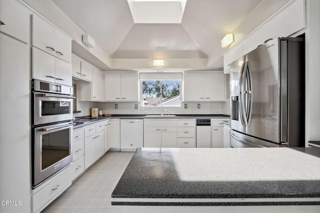 kitchen featuring decorative backsplash, vaulted ceiling, white cabinetry, and stainless steel appliances