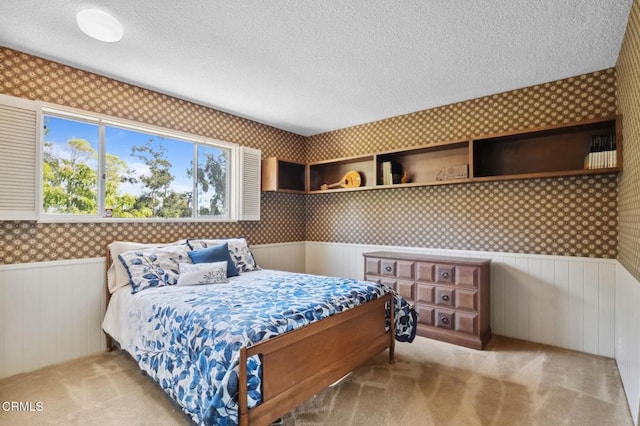 bedroom featuring wainscoting, a textured ceiling, and wallpapered walls