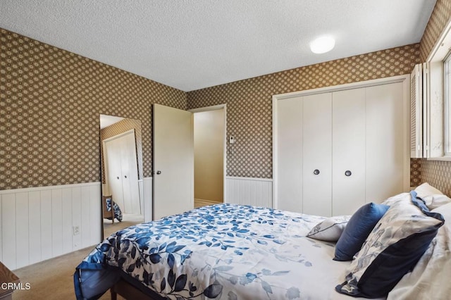 bedroom with wallpapered walls, a wainscoted wall, carpet floors, and a textured ceiling