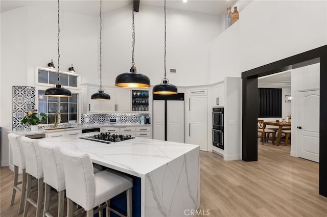 kitchen featuring light wood-style flooring, a sink, decorative backsplash, black appliances, and white cabinetry