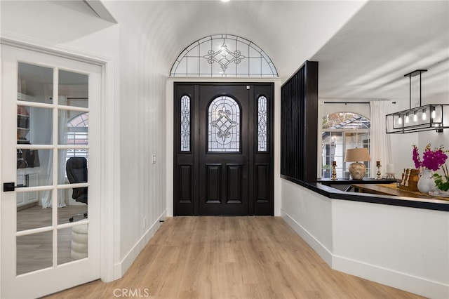 entryway featuring baseboards, a chandelier, and light wood finished floors