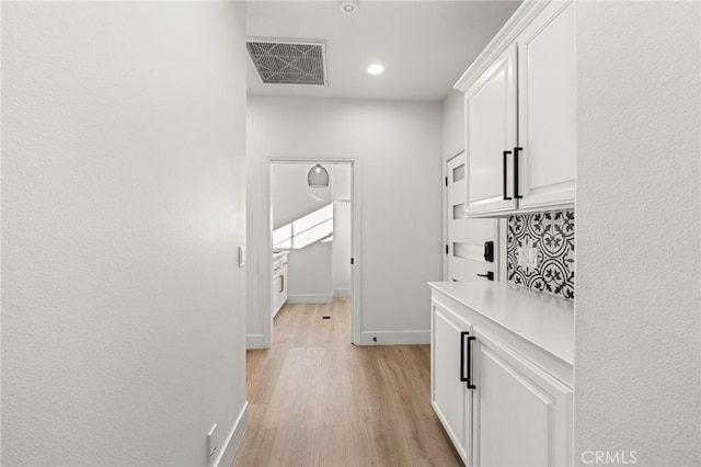 hall with visible vents, light wood-style flooring, and baseboards