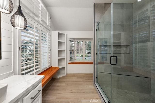 bathroom with vanity, wood finished floors, baseboards, lofted ceiling, and a stall shower