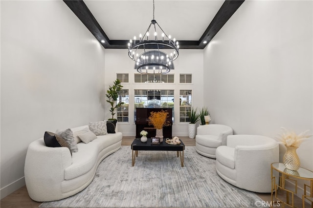 living area featuring wood finished floors, baseboards, a towering ceiling, beamed ceiling, and a chandelier