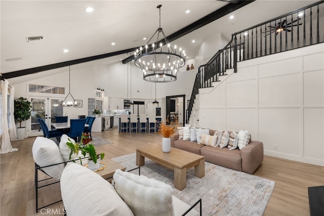 living room featuring visible vents, beam ceiling, a decorative wall, a notable chandelier, and light wood-type flooring